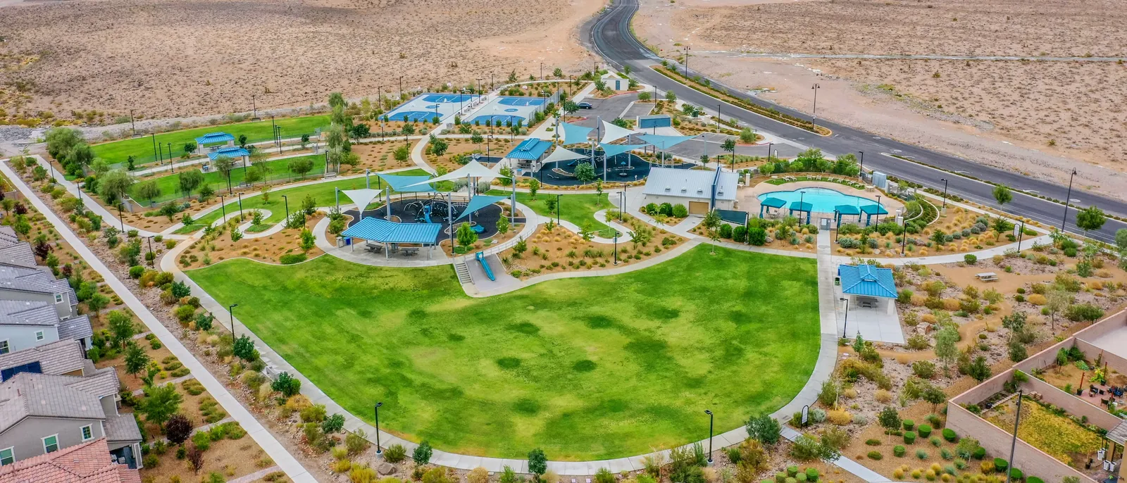 Aerial view of an Inspirada park in Henderson NV — the shared amenities the HOA assessment pays for, including shade-sail playgrounds, a resident pool, pickleball and basketball courts, ramadas and a great lawn