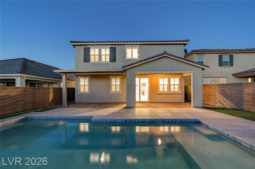 Rear elevation of 2587 Tolmezzo Street lit up at twilight behind the pool