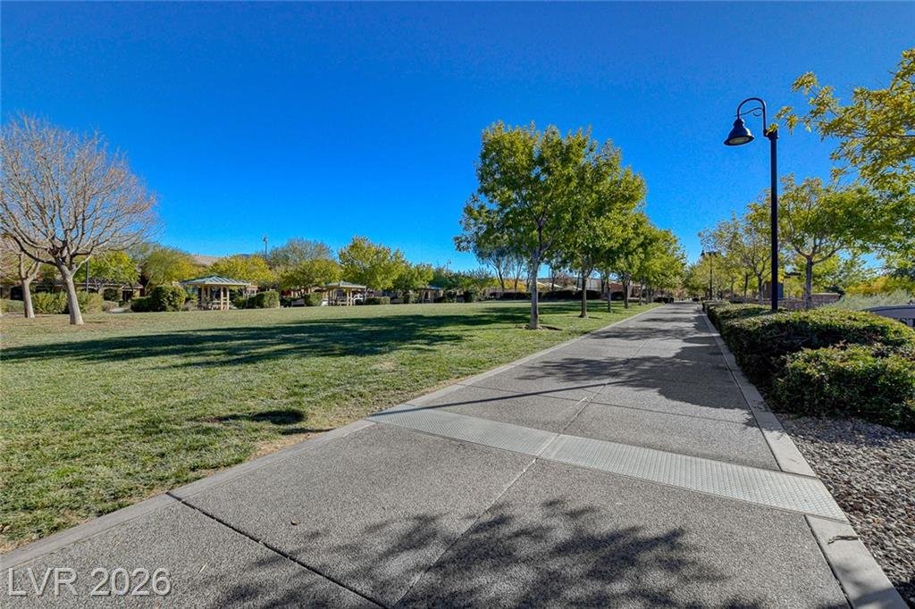 Tree-lined paved path running along a park lawn