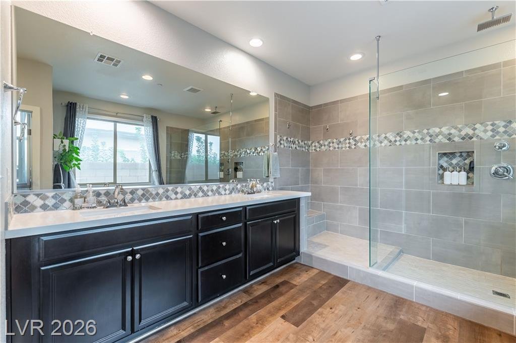 Primary bath dual vanity with dark cabinets and frameless glass shower