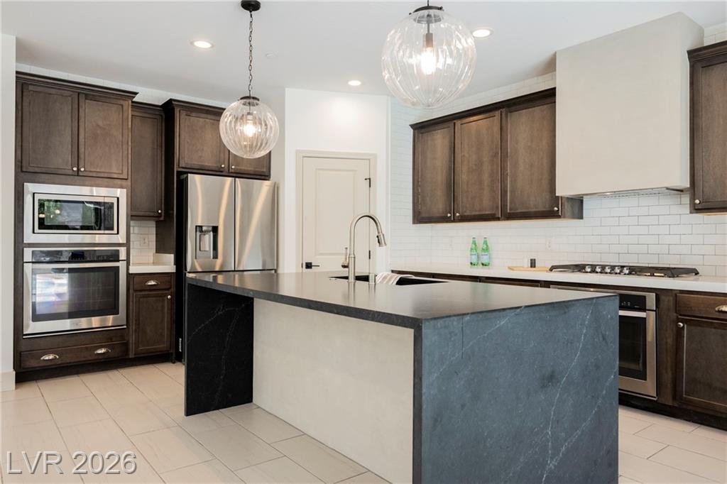 Two-tone waterfall island with dark quartz top, stainless refrigerator and wall ovens