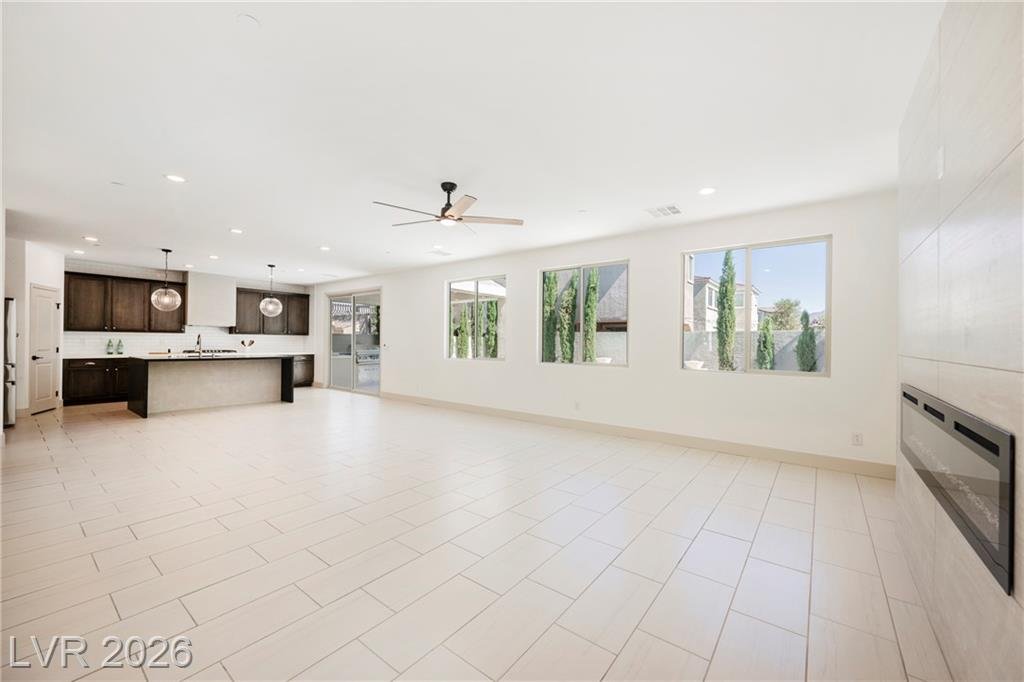 Open great room with tile floors, ceiling fan and the kitchen beyond
