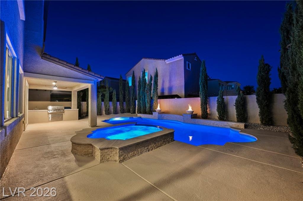 Covered patio, outdoor kitchen and spa lit at night at 2430 Quiet Ode Street
