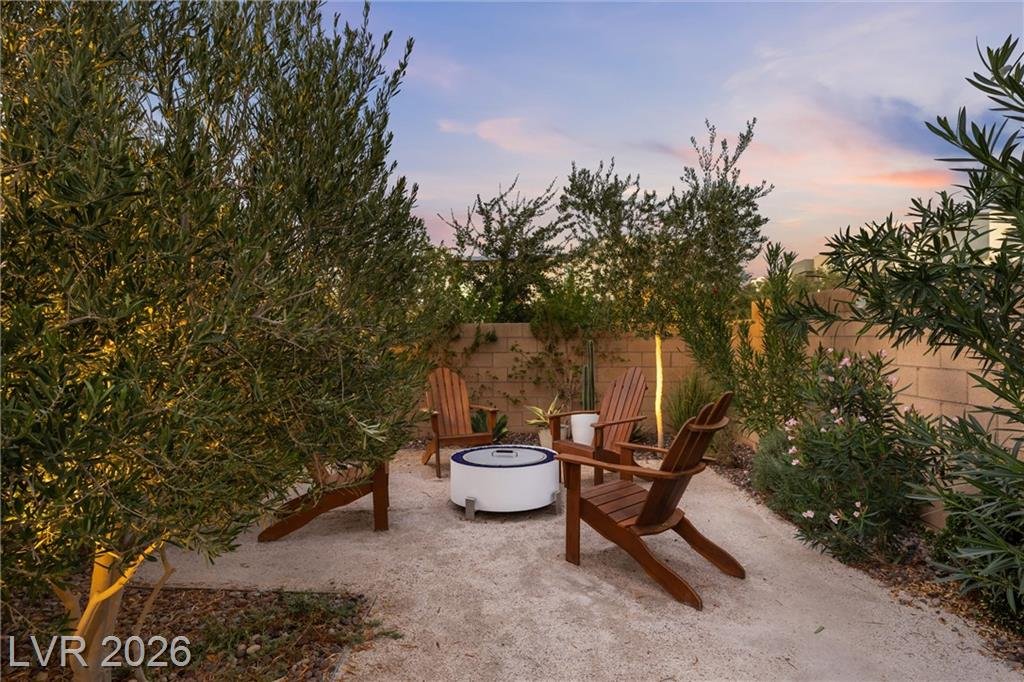 Backyard fire pit with Adirondack chairs under olive trees