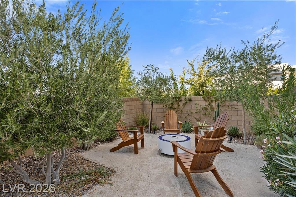 Gravel fire pit area framed by olive trees and a block wall