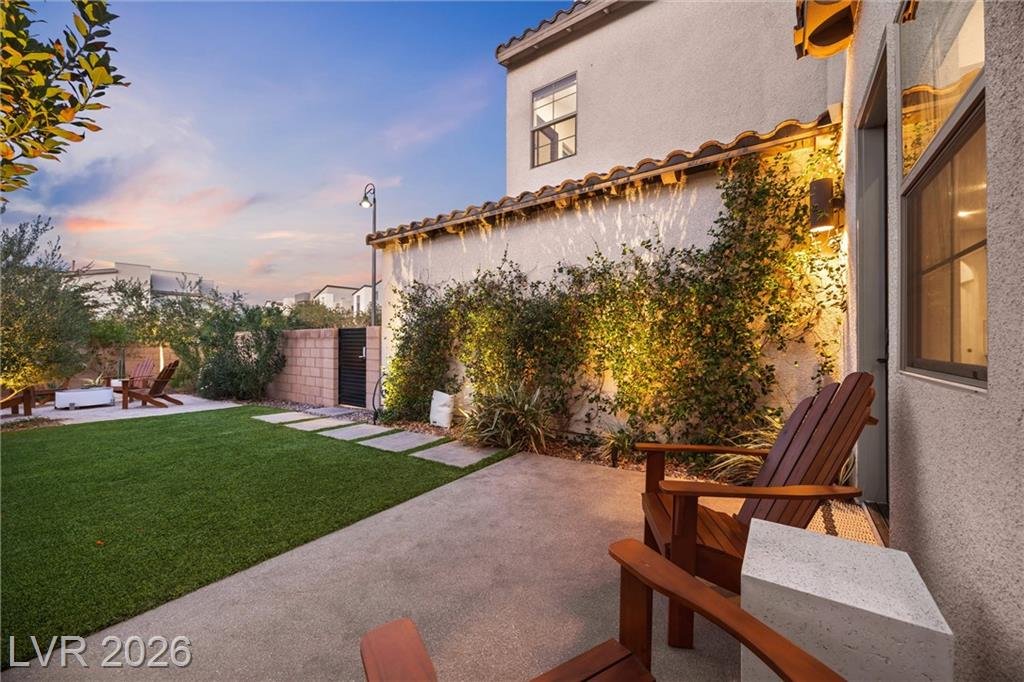 Landscape-lit vine wall along the side yard with turf and patio chairs