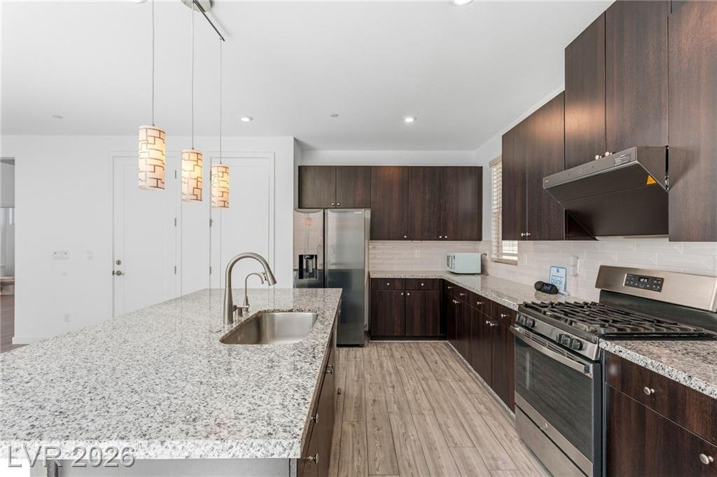 Gas range, stainless hood and white subway tile backsplash with espresso cabinets