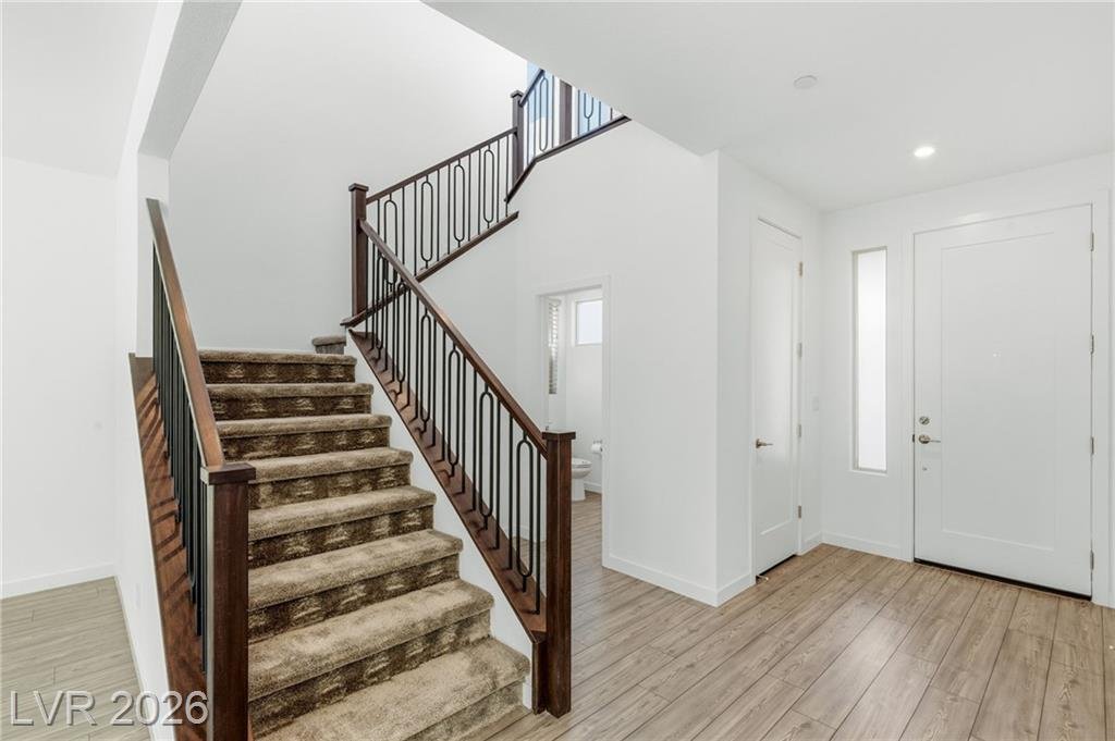 Carpeted staircase with wood rail and iron balusters beside the front door