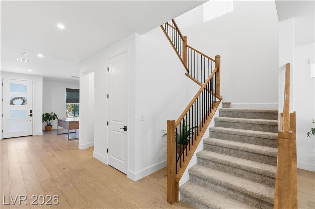Carpeted staircase with wood handrail and iron balusters near the front entry
